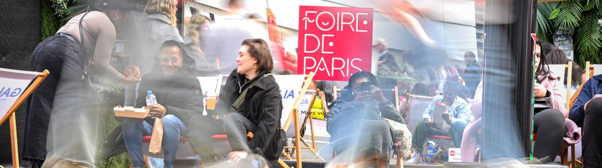 Zone de détente à la Foire de Paris avec des visiteurs assis et un effet de flou sur les passants en mouvement