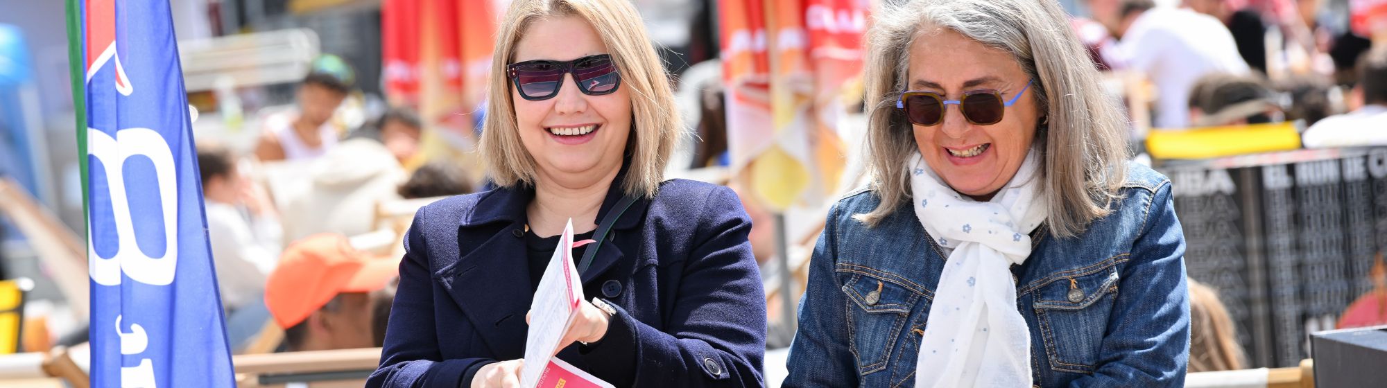 Visiteuses profitant d’un événement en plein air, tenant un flyer d’animation ou de salon grand public