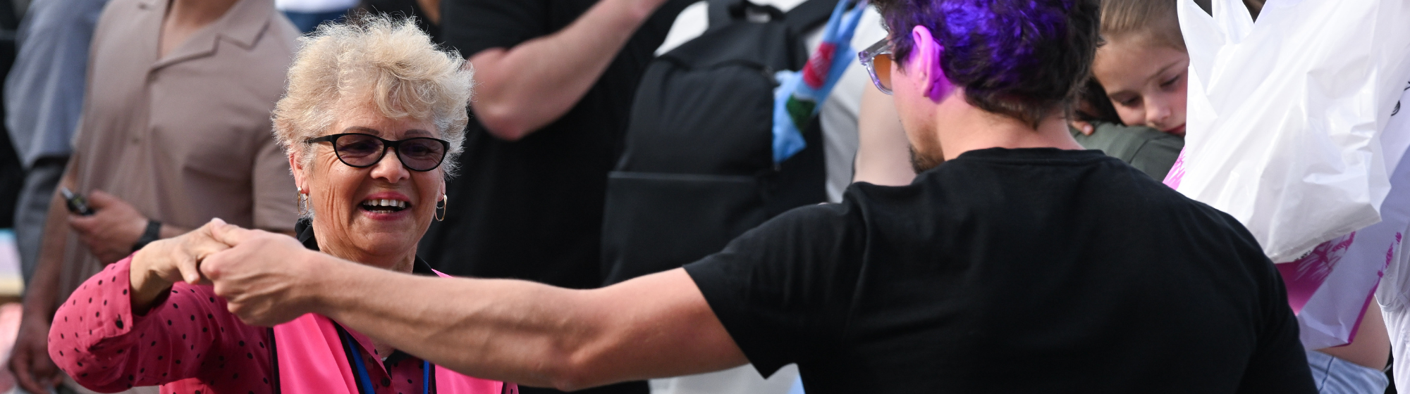 Un homme et une femme portant un gilet rose échangent une poignée de main lors d’un événement en plein air