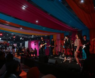 Groupe musical en concert sur scène couverte de tissus colorés, avec un public assis à la Foire de Paris