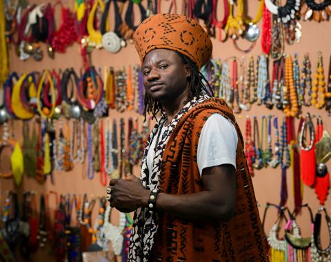 Artisan en tenue traditionnelle sur son stand de bijoux africains à World in Paris