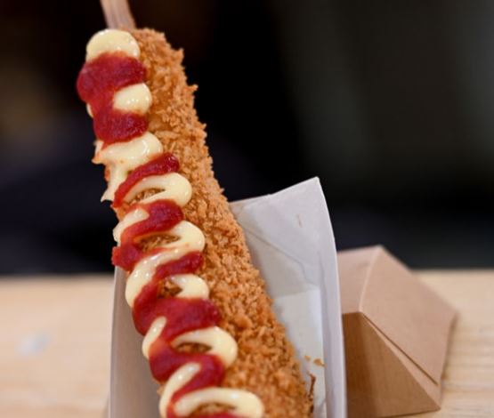 Corn dog croustillant avec ketchup et mayonnaise, présenté dans une barquette en carton