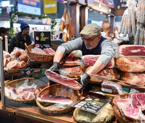 Vendeur sur un stand de charcuterie présentant des jambons et saucissons variés