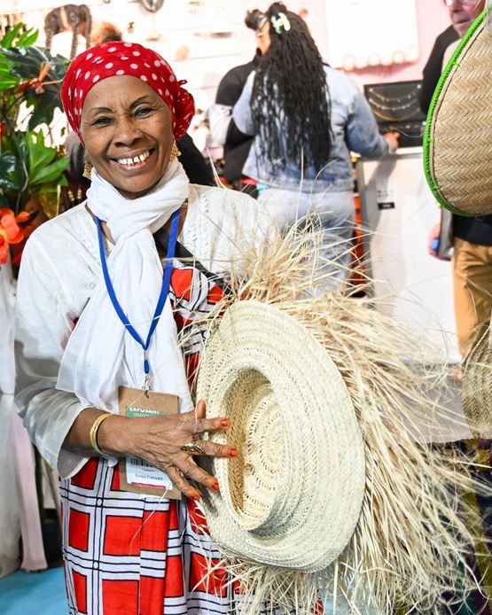 Femme souriante en tenue traditionnelle tenant un chapeau en paille à la Foire de Paris