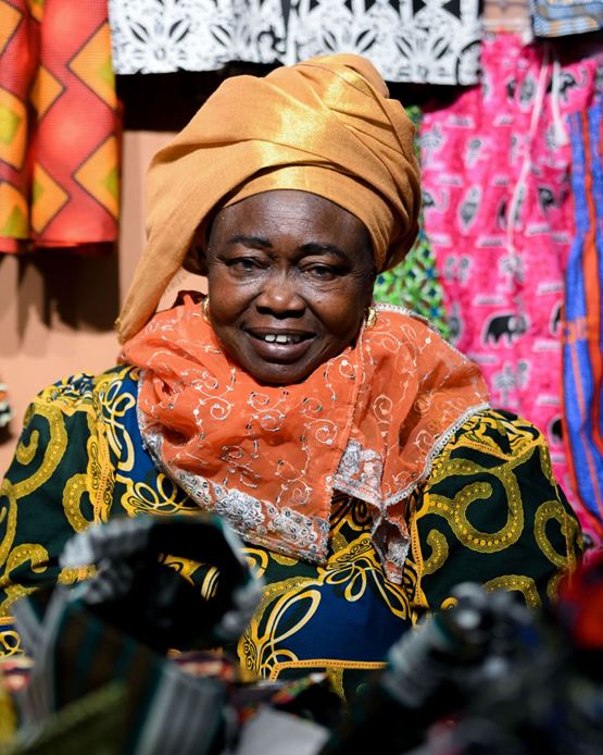 Femme souriante en tenue traditionnelle africaine colorée, au stand de World in Paris