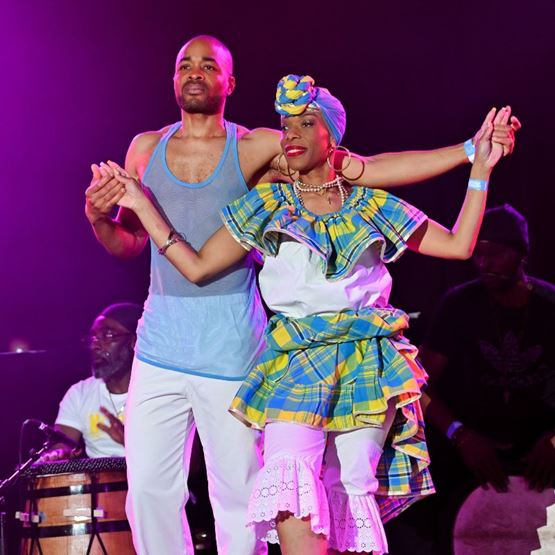 Couple dansant sur scène en tenue traditionnelle antillaise, accompagné de musiciens jouant du tambour