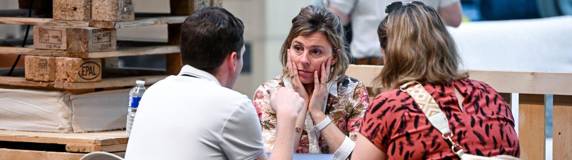 Visiteurs discutant autour d’une table de réunion sur un stand d’architectes avec décor en palettes en bois à foire de paris