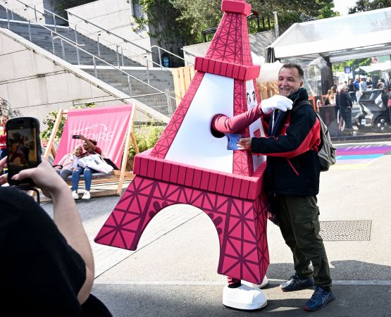 Un visiteur prend une photo avec la mascotte Tour Eiffel à la Foire de Paris pendant qu’un autre groupe se prend en selfie sur un transat