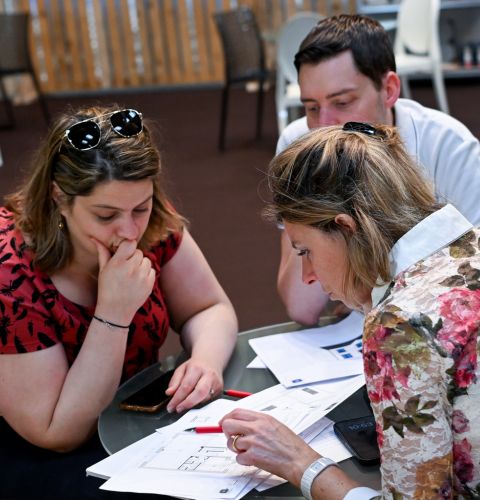 Trois personnes concentrées autour de plans et documents